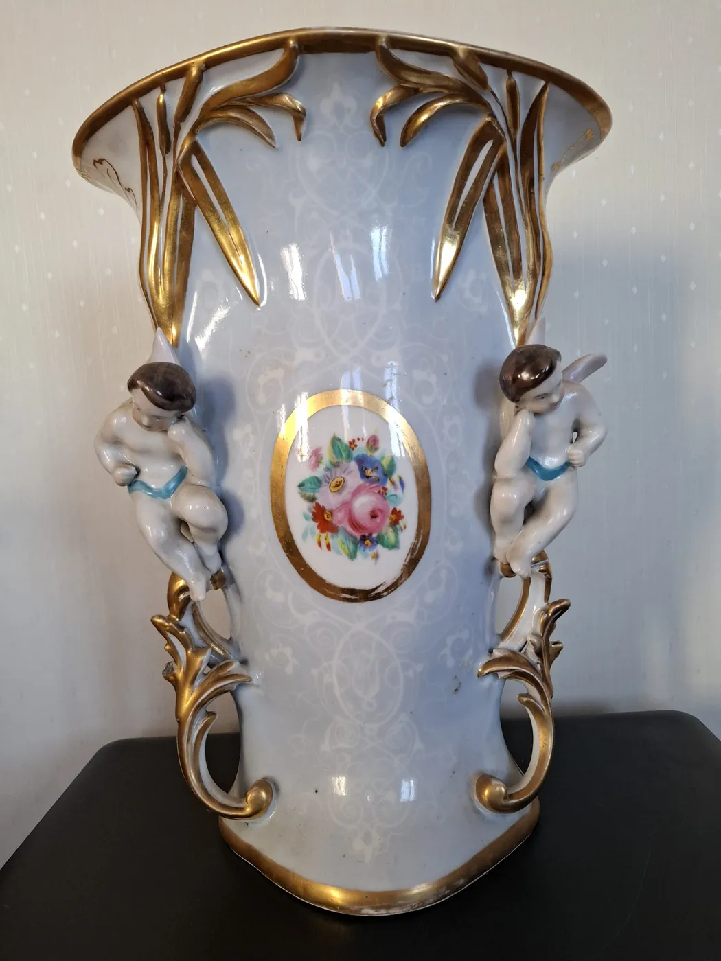 Vase bleu clair à décor doré, orné de deux angelots assis sur les anses et d'un médaillon de fleurs peintes.