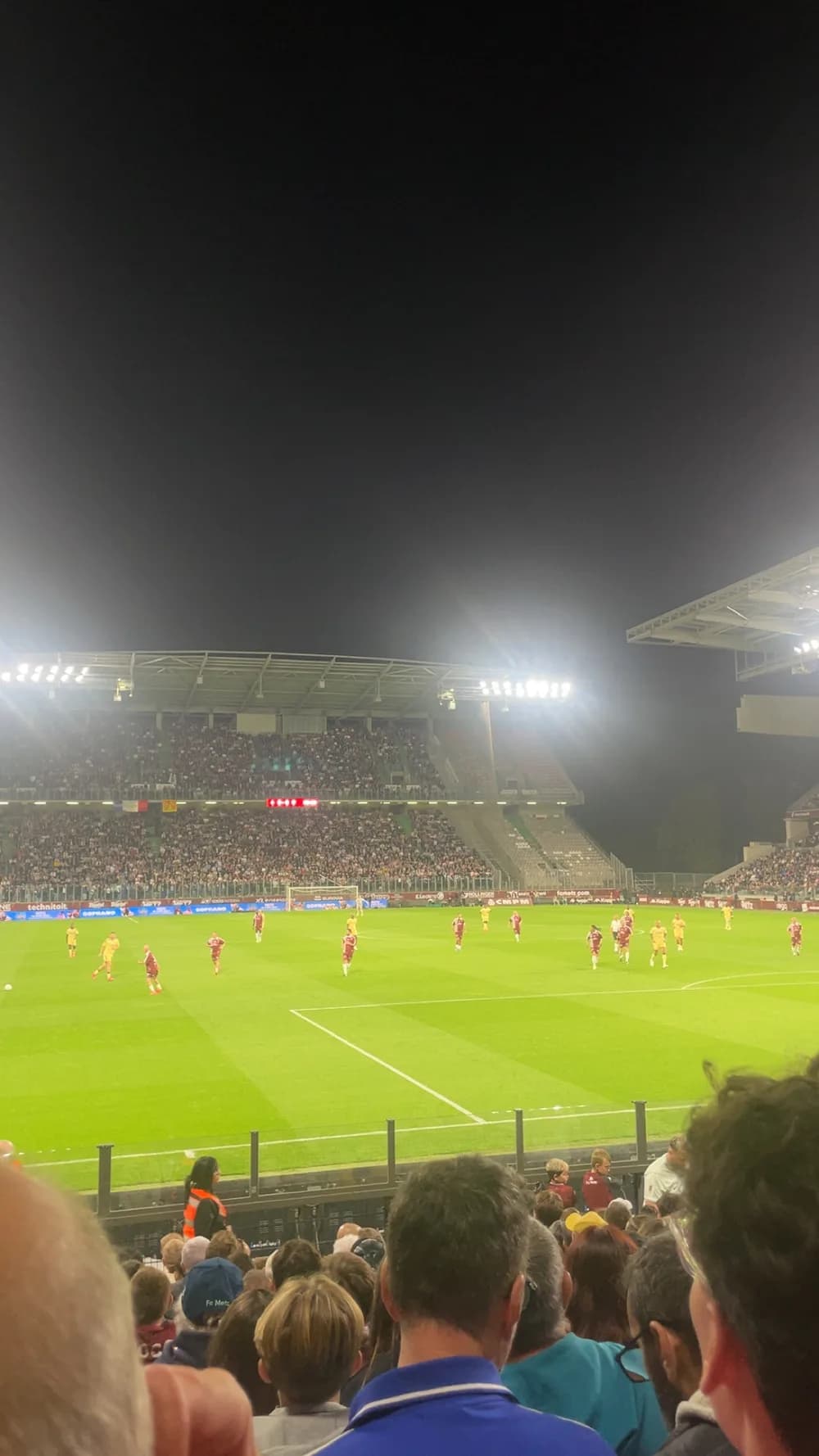 Vue depuis la tribune de Saint-Symphorien pendant le jubilé : la pelouse éclairée, les joueurs et le public au premier plan.