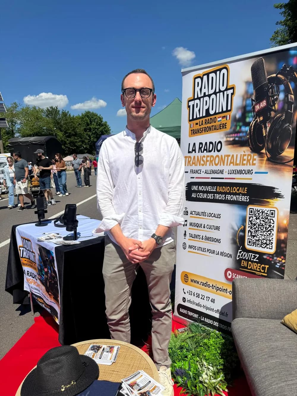 Lucas Grandjean im weißen Hemd vor dem Radio-Tripoint-Stand im Freien, neben dem Roll-up des Senders.
