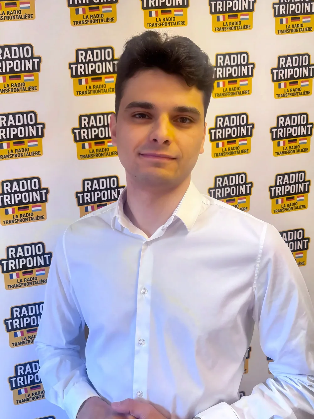 De Martin Beziaud am wäissen Hiem virun der Mauer mat de Radio-Tripoint-Logoen.
